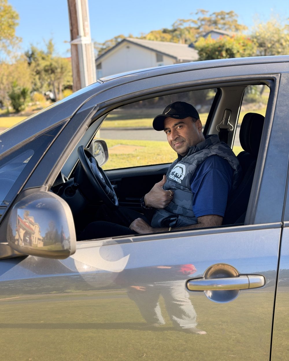 Sam, driving instructor at Uncle Sam Driver Training, seated in the driver's seat giving a thumbs up
